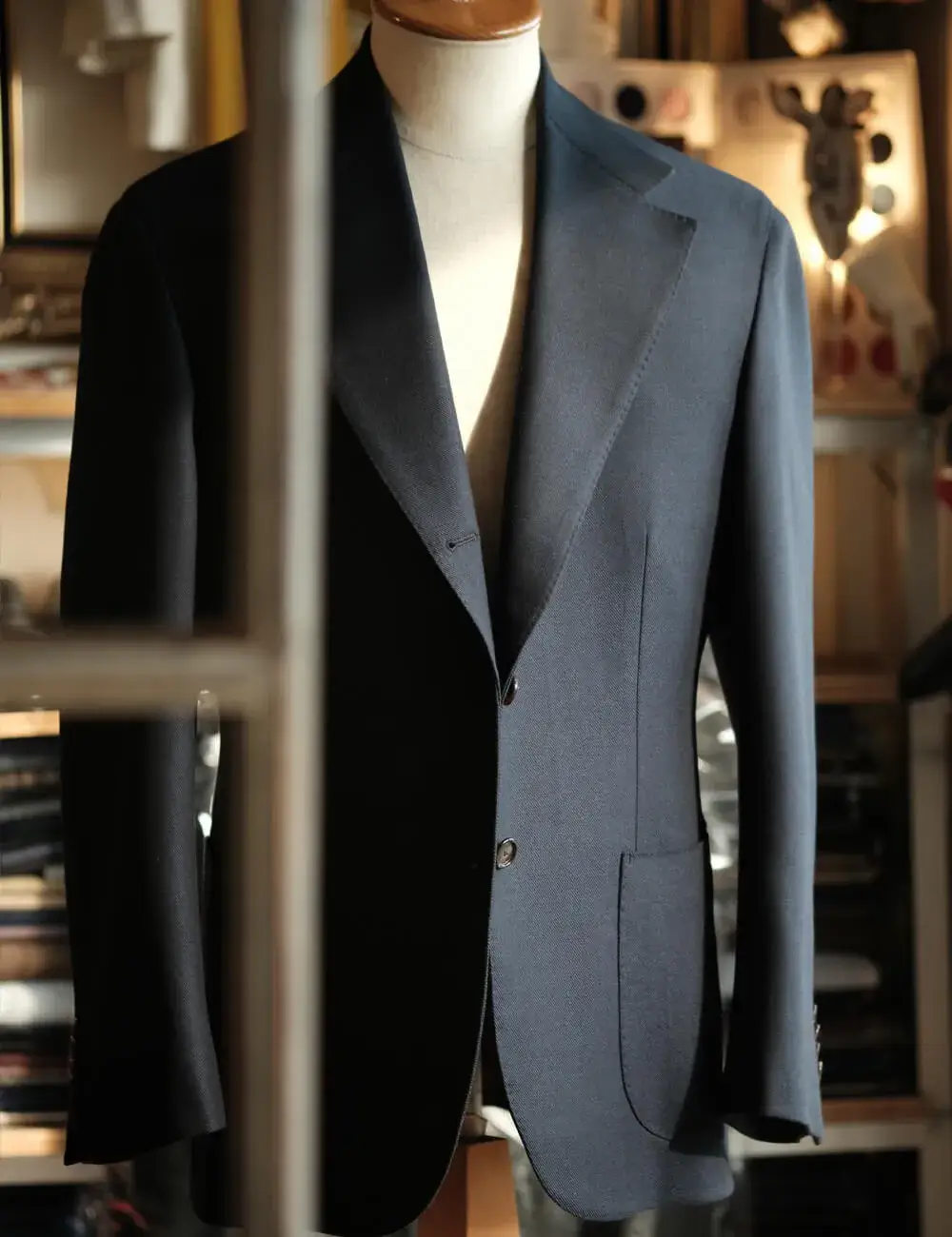 Navy jacket with patch pockets on a tailor's dress form, showing the soft lapel roll of full canvas construction